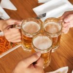 Hands of friends clinking mugs with beer, view from above